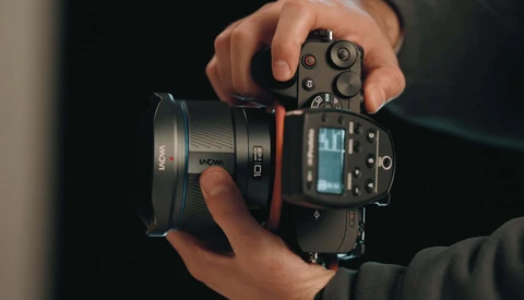 Photographer's hands holding a mirrorless camera with attached lens against a dark background.