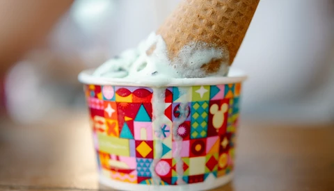 Ice cream cone with white soft-serve frozen yogurt in a colorful geometric patterned paper cup.