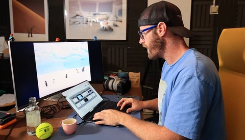 Photographer working at desk with monitor displaying landscape image and tablet for editing.