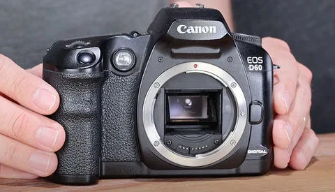 Canon EOS 60D DSLR camera body held in hands showing open mirror box and sensor.