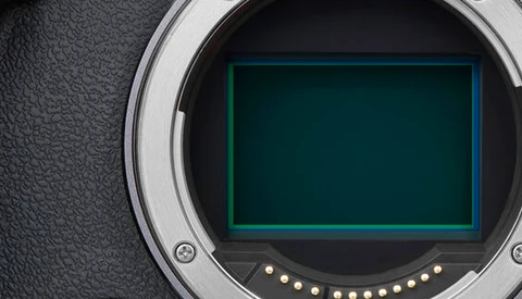 Camera body mirror with open shutter exposing the sensor and cyan-lit mirror box interior.