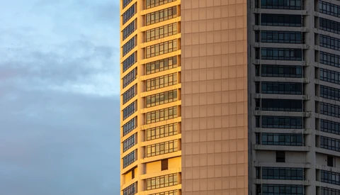 Two residential high-rise buildings with contrasting facades during golden hour, one illuminated in warm yellow tones and one in cool gray tones.
