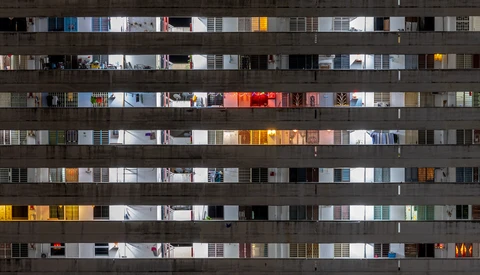 Apartment building facade at night showing illuminated windows across multiple floors with varied interior lighting and decor.