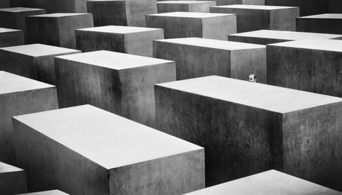 A small figure standing alone among towering concrete memorial blocks in a geometric maze-like formation.