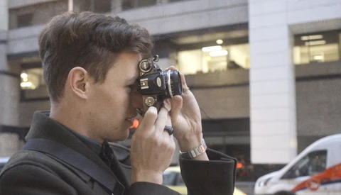 Photographer holding a vintage film camera up to his face to compose a shot outdoors.