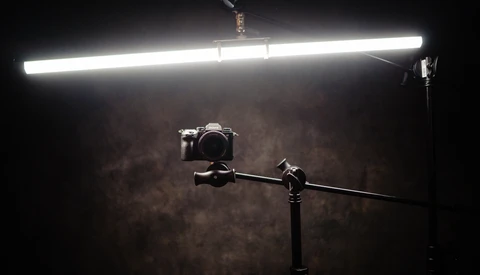 Camera mounted on a boom arm under a bright LED panel light against a textured brown backdrop.