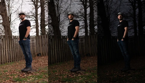 Man in black shirt and jeans standing in wooded area with wooden fence, shown in three progressive lighting conditions from natural to dark.