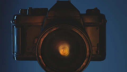 Illustration of a vintage film camera with glowing lens against a blue background.