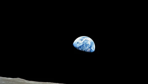 Earth rising above the lunar horizon, illuminated against black space, with textured moonscape in foreground.