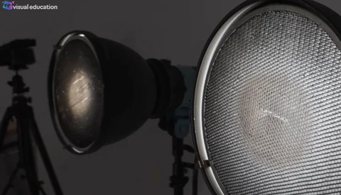Two studio light fixtures with reflectors positioned against a dark gray background, one with visible dome reflector and one with honeycomb grid.