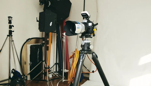 Photography studio setup with tripod-mounted telescope lens, lighting equipment, and camera gear on wooden floor.