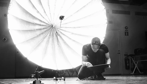 Photographer crouching beside a large circular softbox in a studio setting.