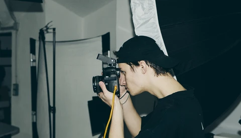 Photographer operating a camera mounted on a tripod with studio lighting setup in an indoor space.
