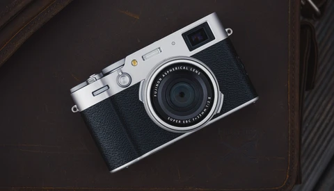 Rangefinder camera with silver top plate and black leather body on a dark textured surface.
