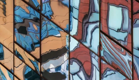 Reflections of blue sky and building facades in glass windows of a modern building.
