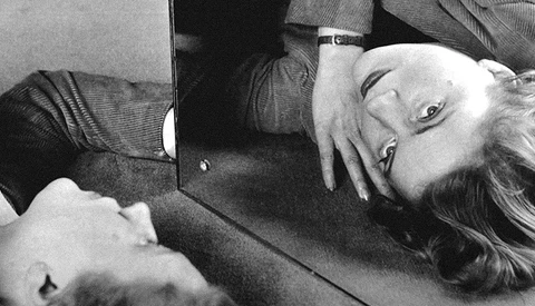Woman lying on floor looking at mirror, black and white portrait photograph.