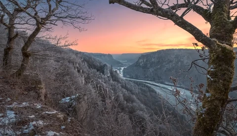 River valley at sunset framed by frost-covered trees and rocky canyon walls.