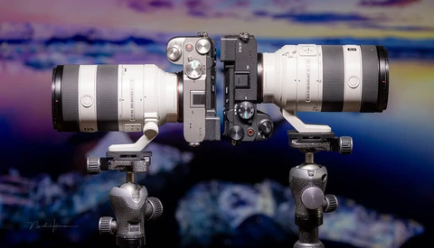 Two telephoto lenses mounted on ball head tripod mounts against colorful sky backdrop.