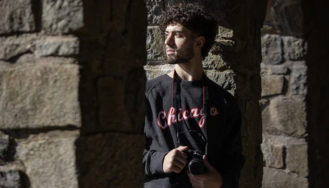 Man holding a camera while standing in shadow between stone walls.
