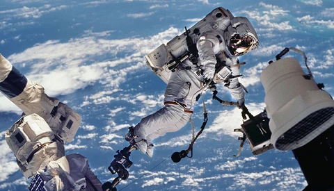 Astronaut performing a spacewalk with Earth and clouds visible in the background.