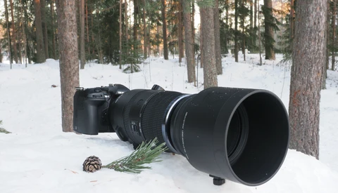 Professional telephoto lens mounted on mirrorless camera body in snowy forest setting.