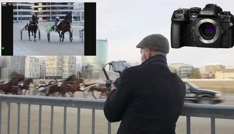 Photographer capturing harness racing from a bridge railing with a mirrorless camera.