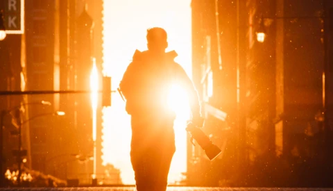 Silhouetted figure walking toward bright golden light between urban buildings at sunset.