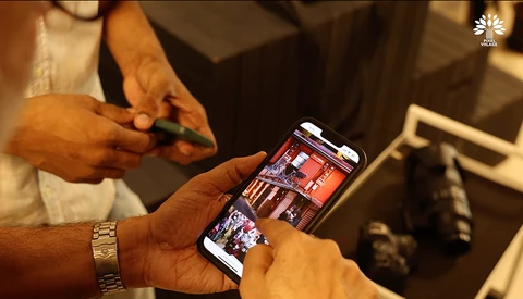Person holding smartphone displaying photo gallery app with warm indoor lighting and blurred background.