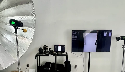 Professional photography studio setup with white umbrella reflector, monitor, and multiple studio lights on stands.