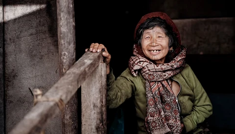 Child in green jacket and red hat smiling while holding a wooden pole or beam.