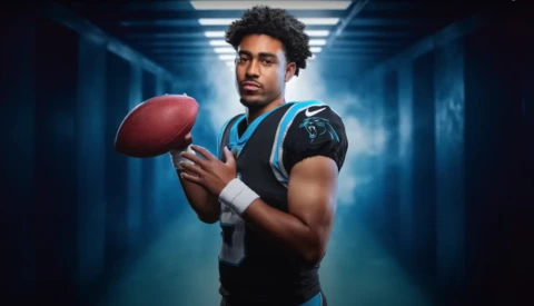 Football player in Panthers uniform holding a football in an illuminated corridor.
