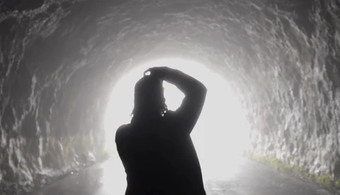 Silhouetted figure standing in a tunnel looking toward bright light at the end.