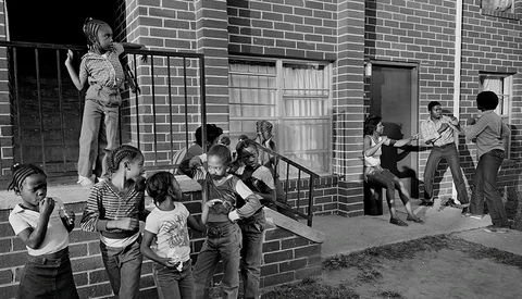 Children playing in an urban alley beside a brick building in this black and white street photograph.