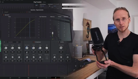 Man holding a microphone in a home studio with a computer displaying audio editing software on the left.