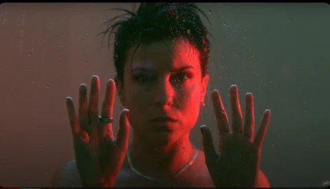 Person with hands pressed against glass, face lit by red and green theatrical lighting.