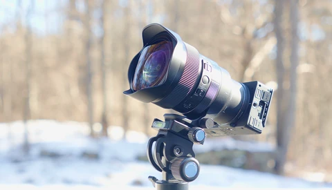 Wide-angle lens mounted on ball head tripod with winter forest background.