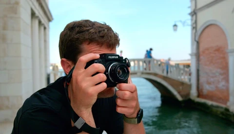Photographer holding a Fujifilm medium format camera up to their face while standing in a European waterside alley.