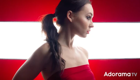 Woman in red strapless dress photographed in profile against red and white striped background.