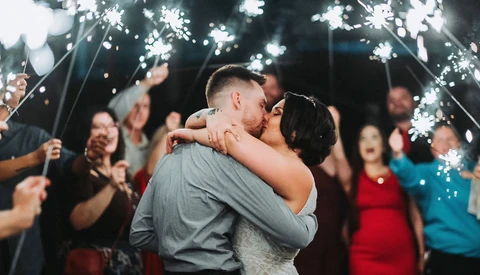 Couple kissing while guests hold sparklers around them at night.