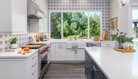 Modern kitchen with white cabinetry, stainless steel appliances, and patterned backsplash overlooking trees through large windows.