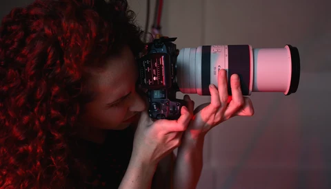 Photographer holding a telephoto lens with pink and red gel lighting creating dramatic side-lighting effect.