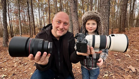 Adult and child holding professional camera lenses outdoors in a forest setting.