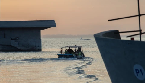 Small fishing boat navigating shallow water between moored vessels at golden hour.