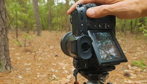 Filmmaker holding a cinema camera with articulating screen in a forest setting.
