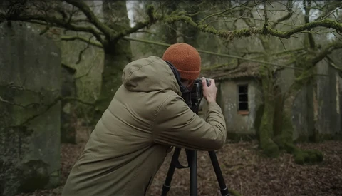 Photographer with camera on tripod shooting in overgrown forest ruins.