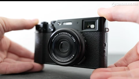 Hands holding a black rangefinder-style digital camera with textured grip and fixed lens.