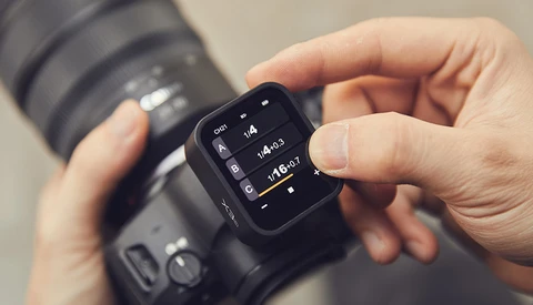 Photographer's hands holding a camera with an external wireless remote trigger displaying exposure settings.