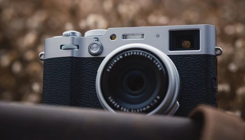 Silver and black rangefinder camera with textured grip, viewed from front against blurred background.