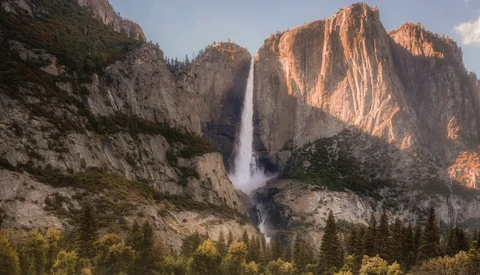 Tall waterfall cascading down a granite cliff face between massive rock formations at golden hour.