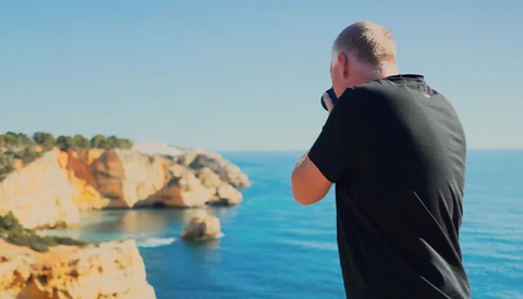 Photographer shooting a coastal landscape with dramatic rocky cliffs and turquoise water.